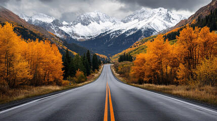 Winding road through an autumn forest lined with golden aspen trees leading to snow-capped mountains under dramatic cloudy skies, capturing the beauty of fall and nature's journey
