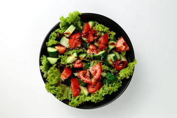 Vegetable salad of tomatoes, cucumbers, onions, lettuce dressed with aromatic dressing in a black plate on a white  background