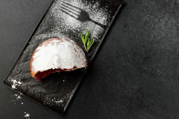 An appetizing donut with strawberries sprinkled with powdered sugar on a black rectangular plate on a gray background