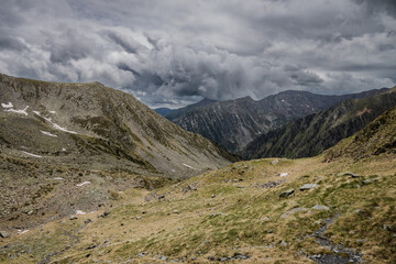 Picturesque landscape on the peak of the mountain with snow and green grass at summer, cloudy in the mountains of Andorra, Arinsal