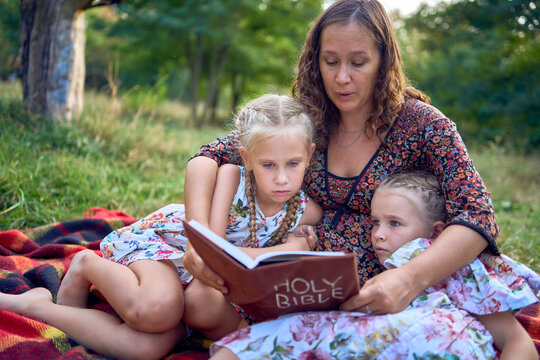 a mother and her two daughters read the holy bible and pray at an Easter picnic