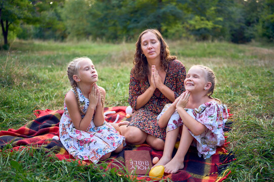 a mother and her two daughters read the holy bible and pray at an Easter picnic