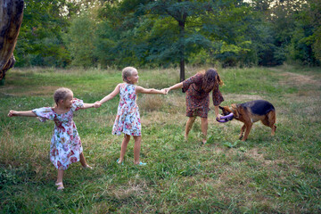 Obraz premium mom and little girls sisters playing with german shepherd dog during easter picnic in the garden