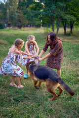 Fototapeta premium mom and little girls sisters playing with german shepherd dog during easter picnic in the garden
