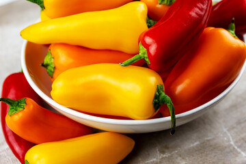 An assortment of red, orange and yellow sweet peppers in a white bowl with a neutral tile background.  Top down view.