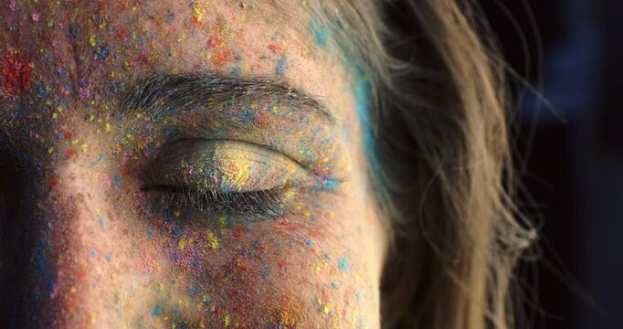 Super slow motion macro of young smiling woman eye covered with rainbow colors colorful powder isolated on dark background at 1000 fps.