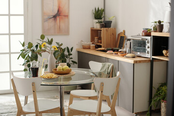 Three chairs surrounding glass kitchen table with vase, two drinks with straws, french fries on plate and bowl with ripe apples