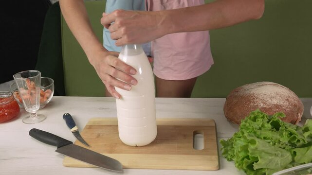 Hands of young woman european unscrews the cap of a bottle of milk, front side view medium shot. Beverage concept, cooking at home, refreshing drinks, healthy eating