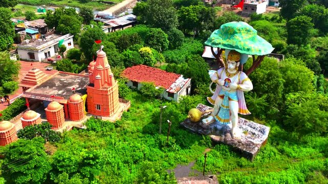 drone shot of The statue of God Hanuman stands next to the temple, surrounded by lush green trees in madhye pradesh
