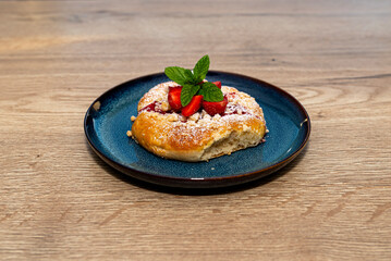 Handmade yeast cake with strawberries and pudding, lying on a blue plate.