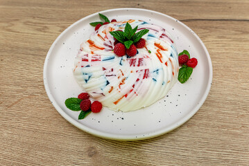 Dessert made of white and colored jelly, decorated with mint leaves and raspberries..