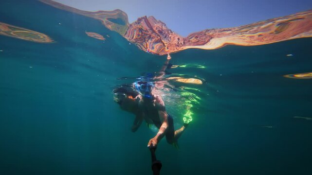 Couple diving underwater, man and woman swimming underwater with mask, snorkel and fins holding hands and filming themselves on camera, vacation selfie, slow motion