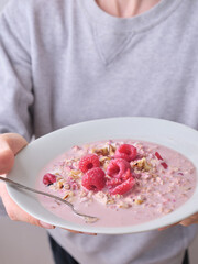 Overnight oats with raspberries and hazelnut topping. Female model holding a bowl of healthy breakfast