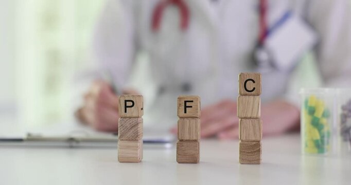 Letters PFC on wooden cubes stacks against doctor filling form in hospital. Medical specialist in uniform prescribes medication to patient