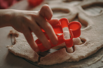 A child's hand pressing a red cookie cutter into dough. The cutter has a gingerbread figure. The...