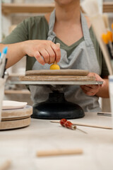 Girl is working with a sponge on a stick to shape pottery and absorb excess water from clay. Using wooden handle sponge to smooth the surface of a clay product in a pottery workshop.
