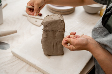 Girl is using a wire cutter to cut off a piece of clay before modeling the product. Slicing off a chunk of clay from a large block using a sharp wire clay cutter.