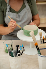 Using a brush to paint a ceramics bowl. Learning how to paint a handmade pottery project. Girl is...