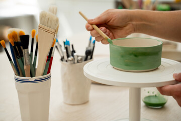 Using a brush to paint a ceramics bowl. Learning how to paint a handmade pottery project. Girl is...