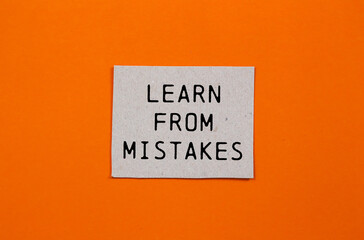 Learn from mistakes message written on paper piece with orange background. Conceptual learn from...