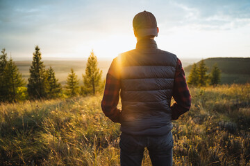 A solitary man stands in the midst of a vast, open field, gazing up at the warm rays of the sun while becoming deeply immersed in the stunning beauty of the surrounding nature