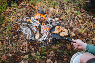 A person is skillfully cooking delicious dishes over a campfire in the peaceful woods, surrounded by stunning nature and the delightful aromas of food wafting through the air