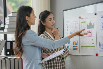 Two businesswomen having a discussion about financial data while pointing at charts on a whiteboard © amnaj