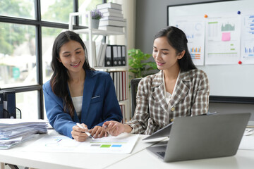Obraz premium Two asian businesswomen are having a discussion over financial charts and reports using laptop at the office