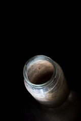 Empty, dirty glass jar on a black background, with stains and shadows, high angle