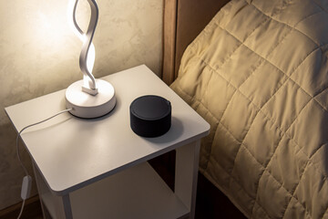 Smart speaker or white noise generator on bedside table in bedroom. Smart device for sleeping