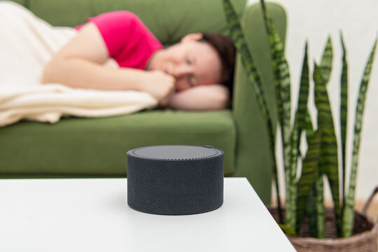 Smart speaker or white noise generator on bedside table. Woman is sleeping on green sofa