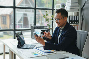 Asian businessman is having a video call on his smartphone in a luminous office