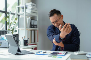 Asian businessman experiencing sudden elbow pain while working at his desk in the office