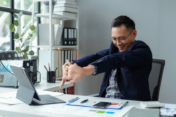 Tired businessman takes a break at his office desk, stretching for health and wellness. Movement and exercise help him balance work and life, staying happy and productive