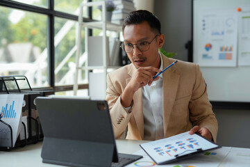 Obraz premium Businessman is reviewing financial reports and using a tablet for a video conference in the office