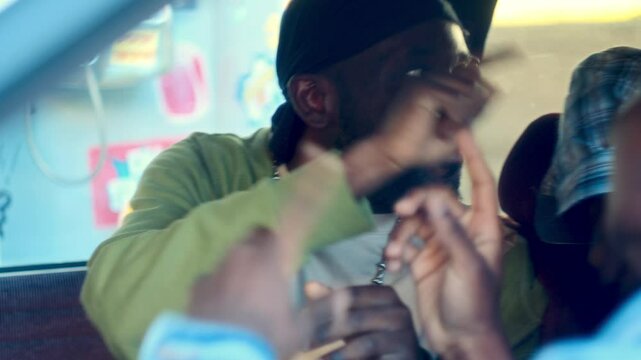 Smiling African American man wearing durag, silver chain and casual outfit sitting in the car and chatting with friends as having fun and chilling together