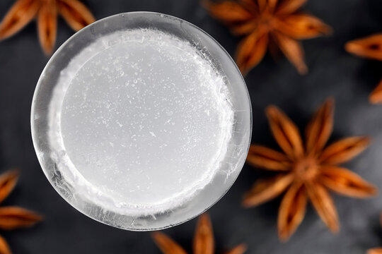 Top view of iced ouzo served in an ice shot glass isolated on a black slate plate among star anise fruits, close-up of an anise-based distilled spirit with louche effect