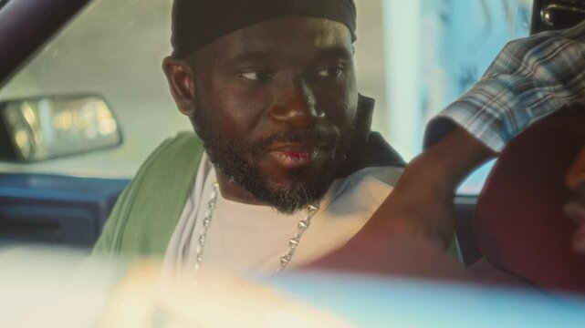 Black man wearing durag, silver chain necklace and hip hop style outfit having lively discussion with friends, smiling and having fun as chilling together in the car