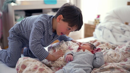 Older brother lying on the bed face-to-face with newborn sibling, sharing an intimate moment of connection and bonding, representing the beginning of a lifelong sibling relationship