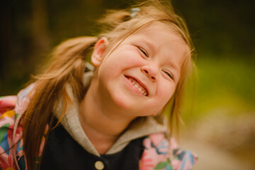 Naklejka premium Portrait of a small girl with ponytails in a jacket. Grimaces. Emotions. Autumn