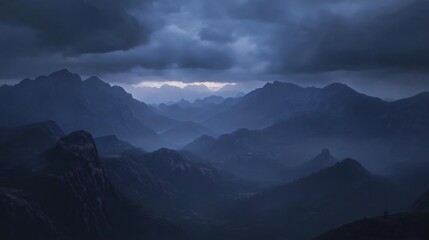 A dramatic mountain range enveloped in mist, with dark clouds overhead and faint sunlight.