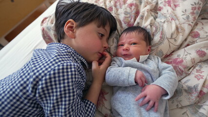 Obraz premium Older brother lying side by side with newborn sibling on a bed, sharing a close and heartwarming moment of bonding that emphasizes the love and affection between the two siblings