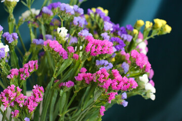 Bouquet of multicolored flowers in a vase (Limonium sinuatum, Statice sinuata) on a green background