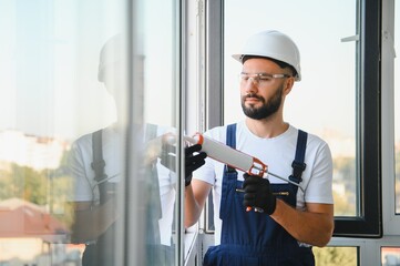 Worker sealing plastic window with caulk indoors. Installation process
