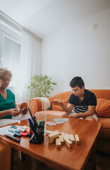 Obraz premium A grandmother and her grandson play a card game in a warm living room, surrounded by family-friendly decor, encouraging love and bonding through playful interaction.