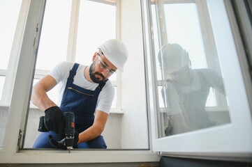 handyman adjusting white pvc plastic window indoors. worker using screwdriver to repair upvc window. homework maintenance