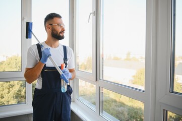 Caucasian handsome man, worker of cleaning service, in blue overalls and in a cap, blaser, Cleaning, washing Windows by special mop, enjoying his work. High quality photo