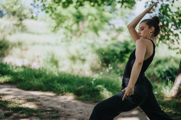 Lovely girl dancing in nature, displaying a graceful modern dance performance outdoors among lush greenery
