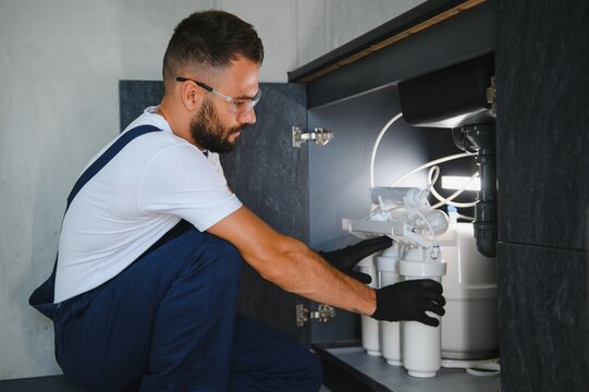 Plumber installs or change water filter. Replacement aqua filter. Repairman installing water filter cartridges in a kitchen. Installation of reverse osmosis water purification system