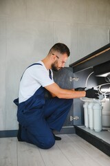 Plumber working install new cartridge for cold water filter in white kitchen